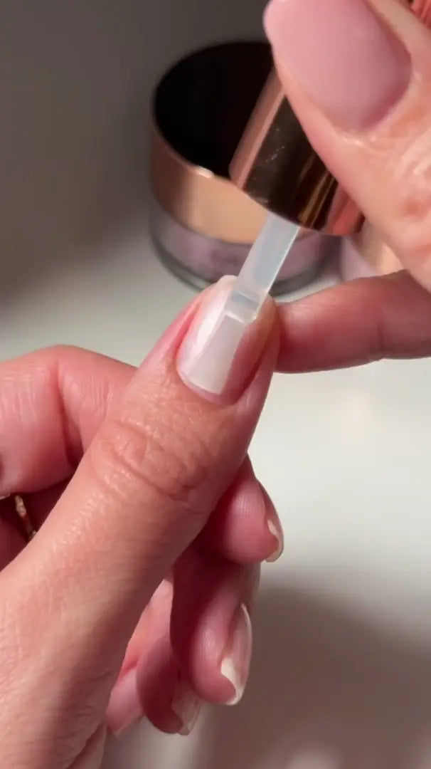 Een transparante nagellakkwast met metalen handvat brengt een glanzende topcoat aan per diplaag