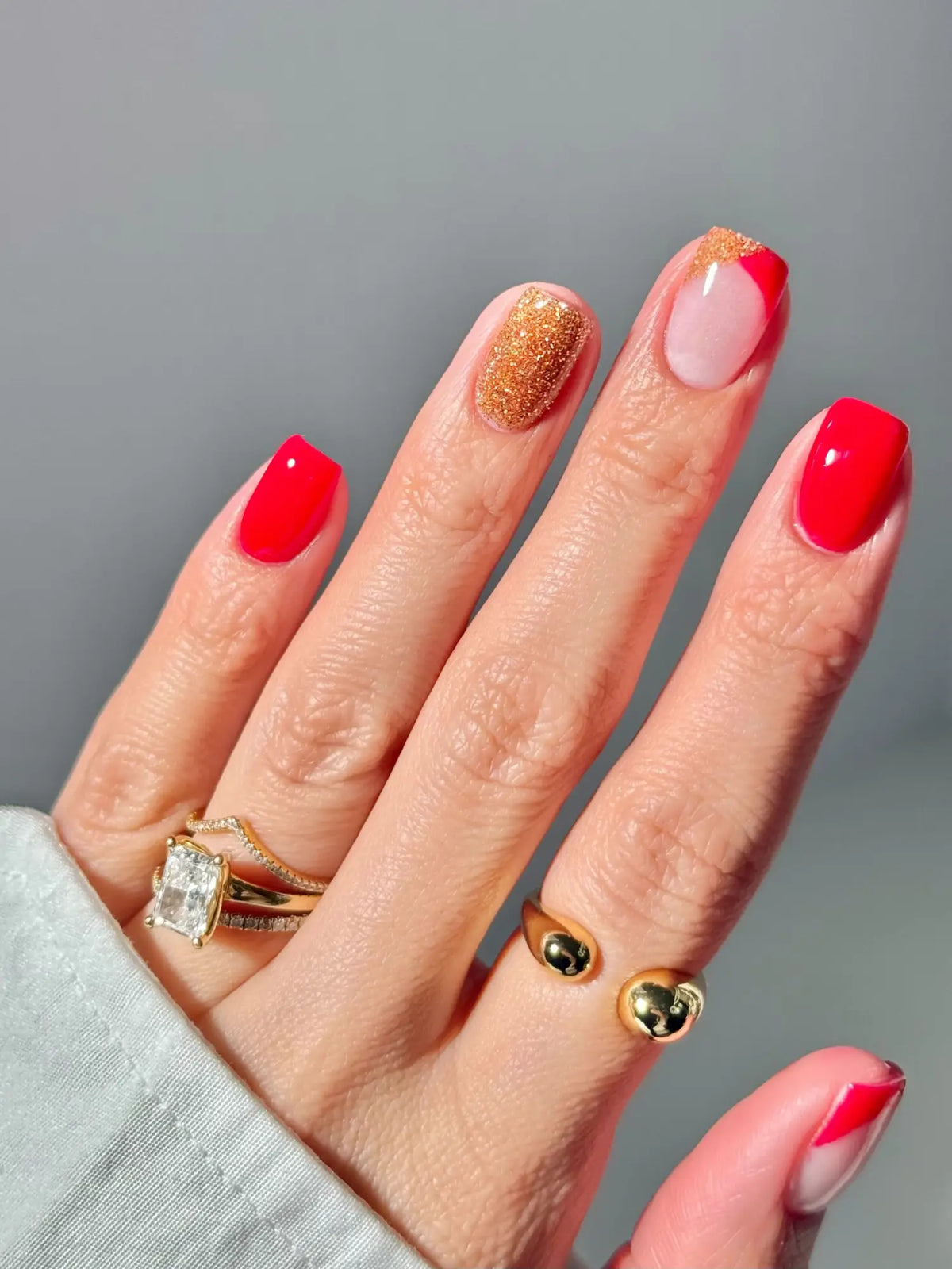Een hand met felle rode, gouden glitters en roze gelnagels in een moderne french tip stijl in een artikel over gelnagels.