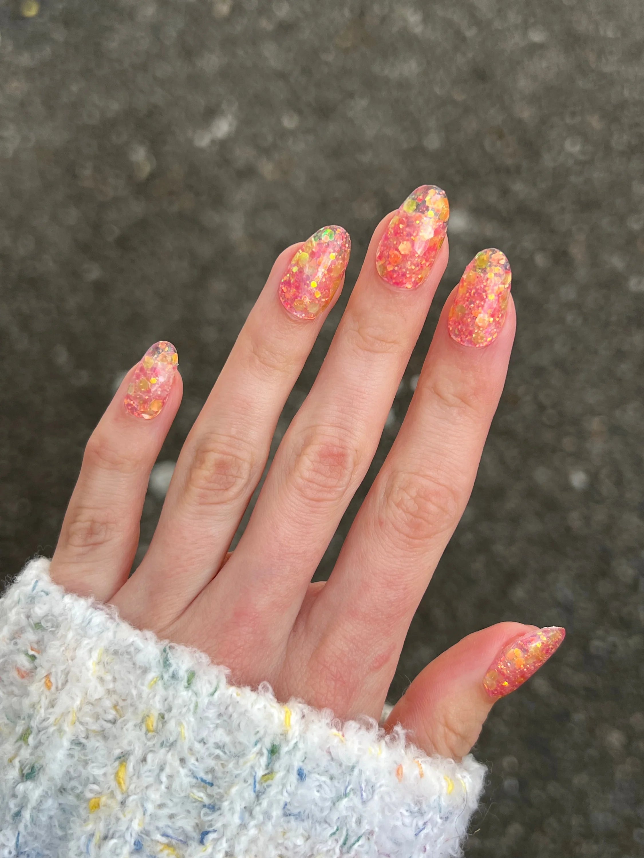 Een hand met lange amandelvormige nagels bedekt met levendige oranje en gele glinsterende golden rose dipping powder