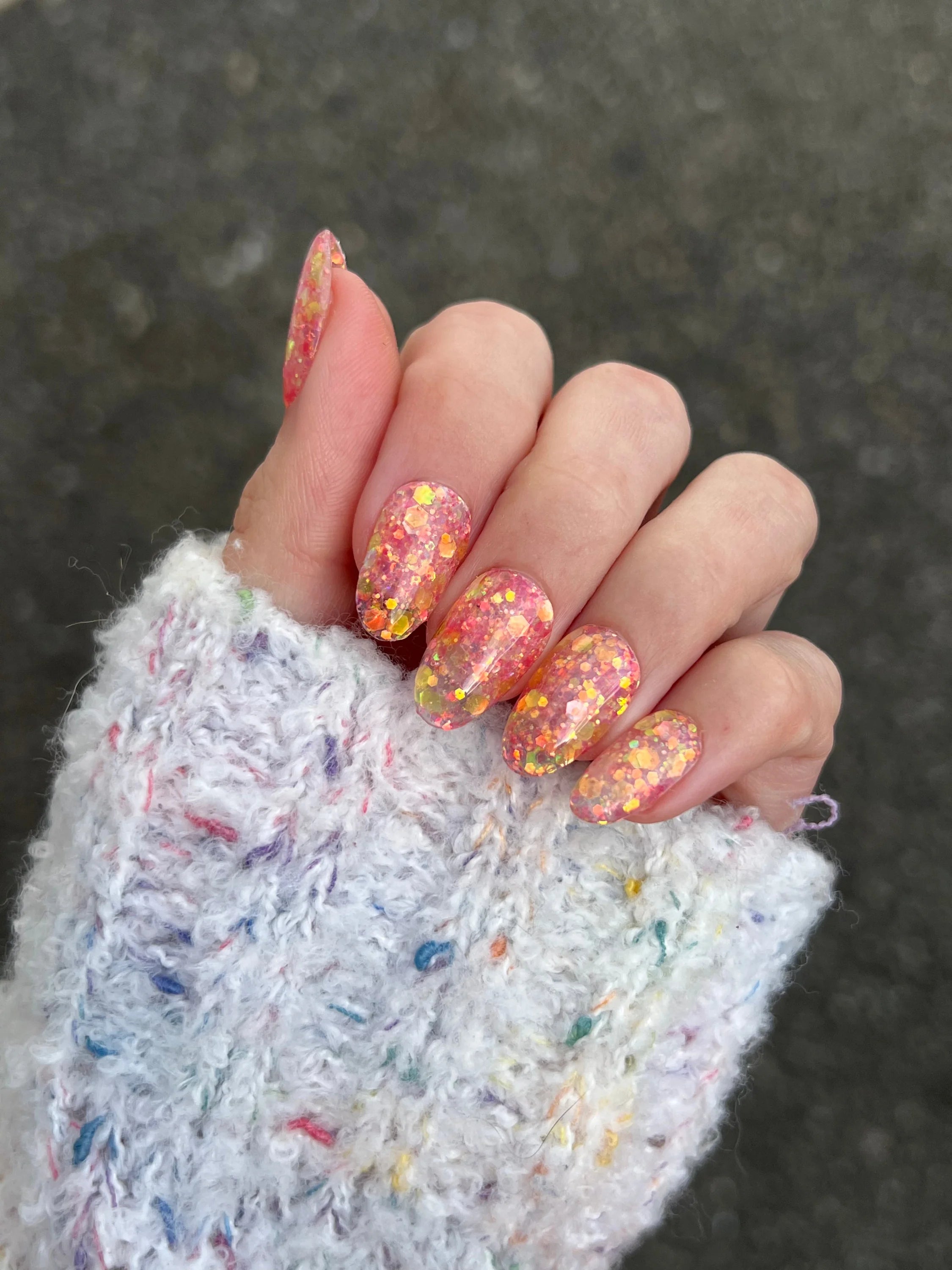 Hand met nagels gelakt in sprankelend oranje en geel glitter gellak met golden rose dipping powder