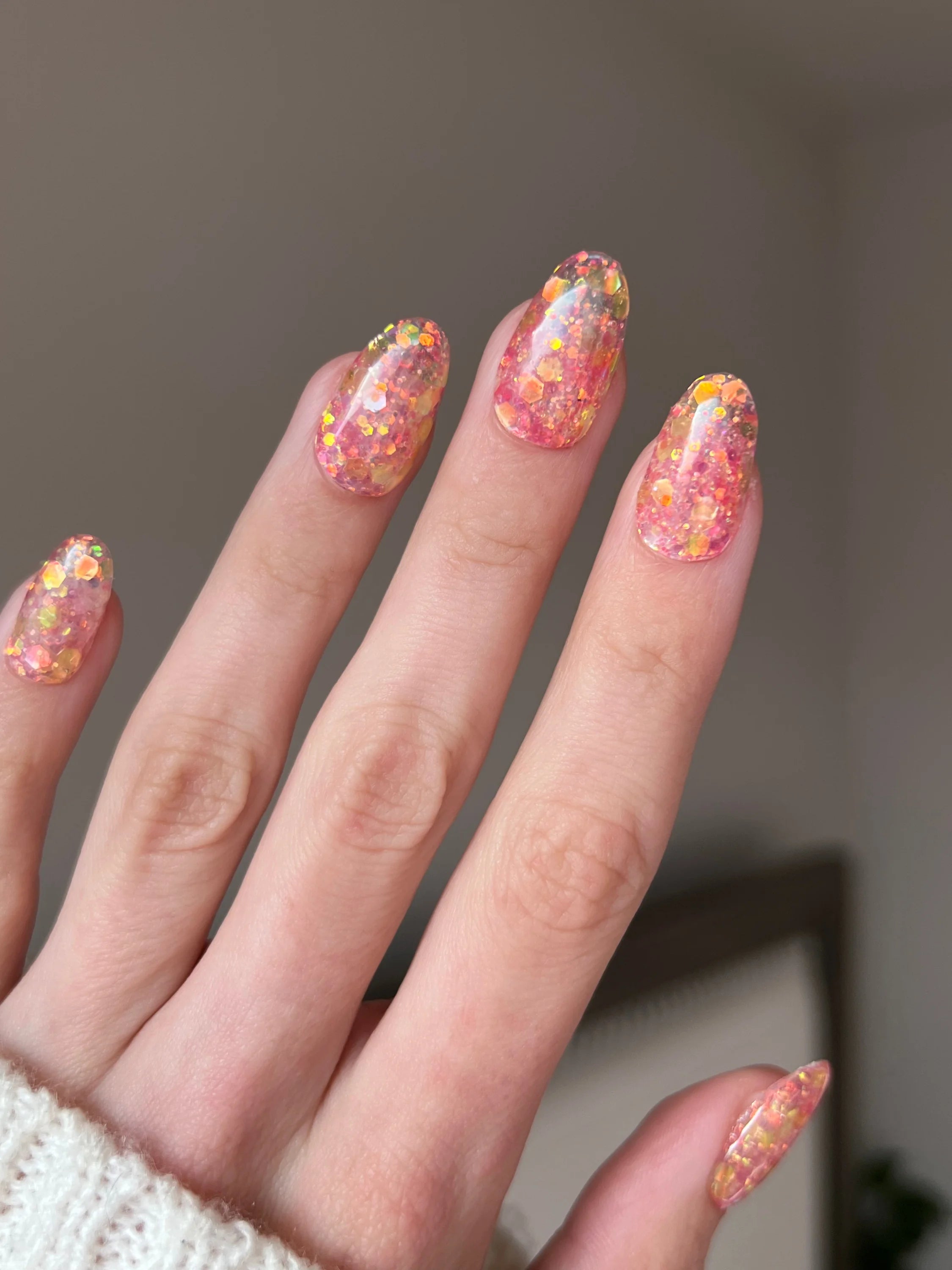 Hand met lange amandelvormige nagels met een glinsterend roze en gouden glitterdesign met golden rose dipping powder
