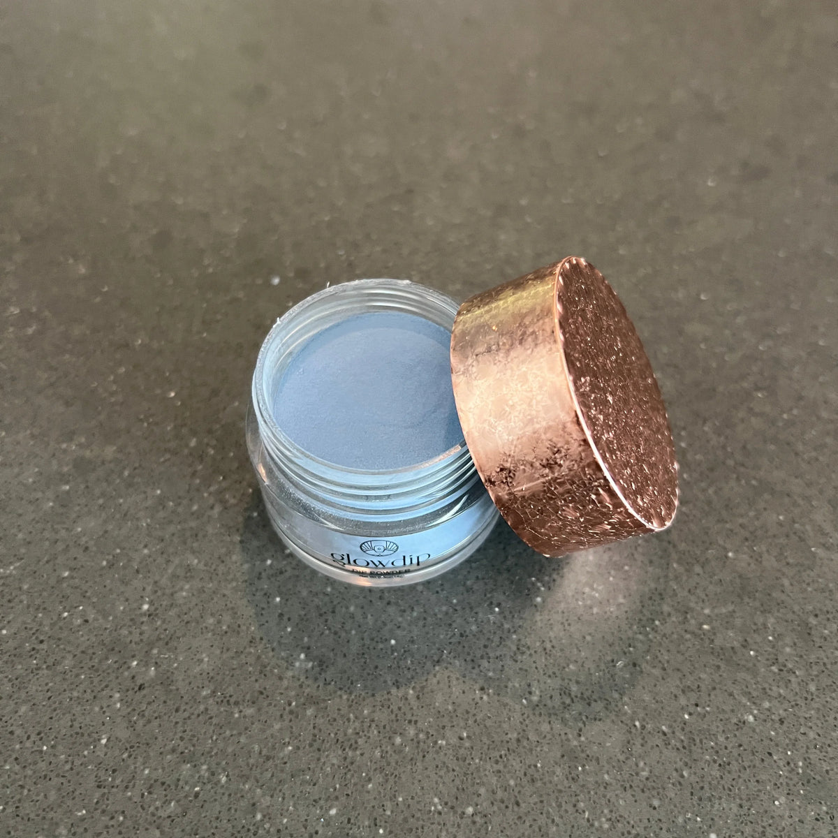 Een helder glazen potje met een glanzend roségouden deksel en lichtblauw dippoeder limited edition 10 moon glow
