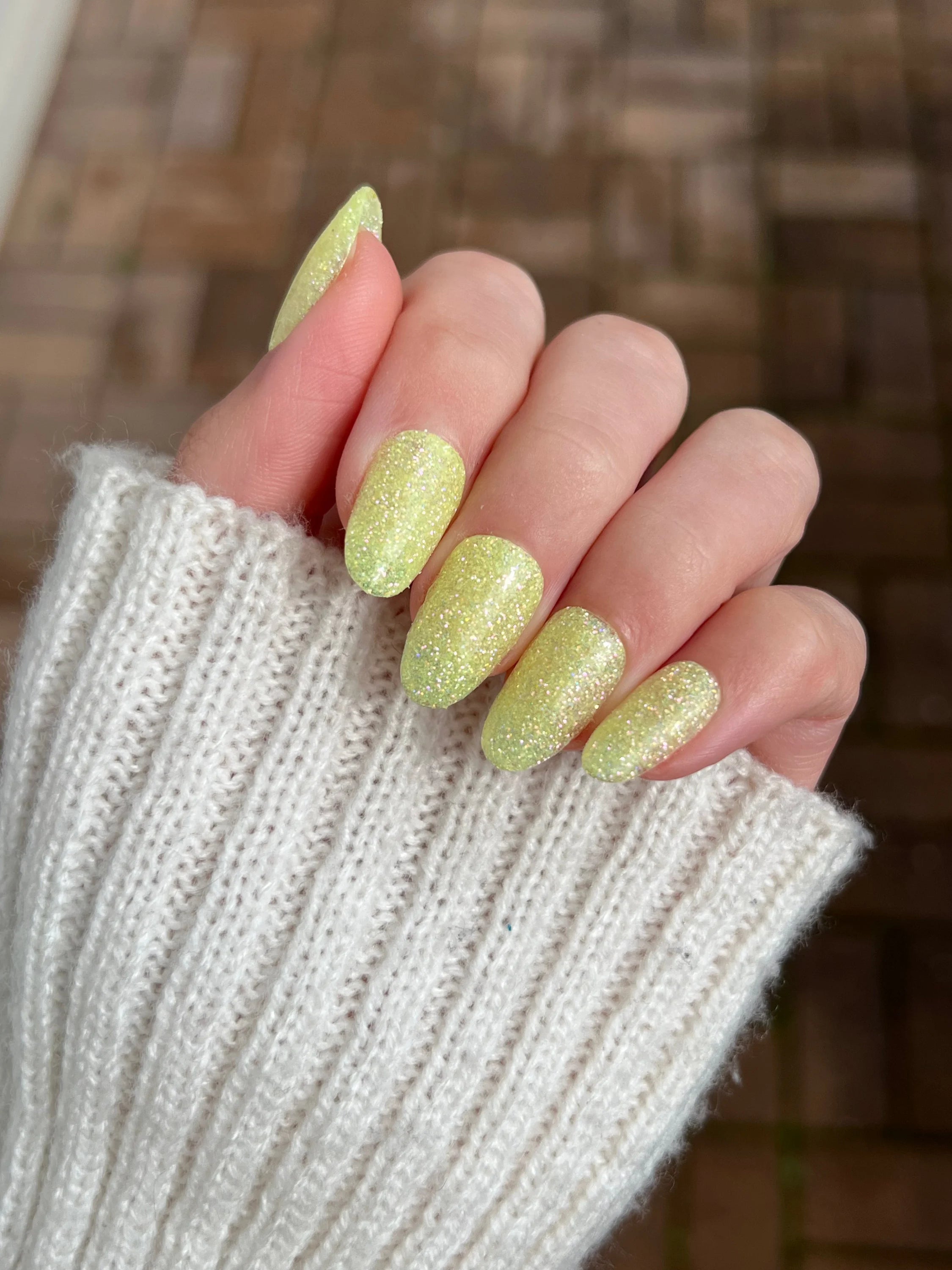 Hand met lange amandelvormige nagels gelakt in glinsterende bleke gele glitter lemon fizz dipping powder