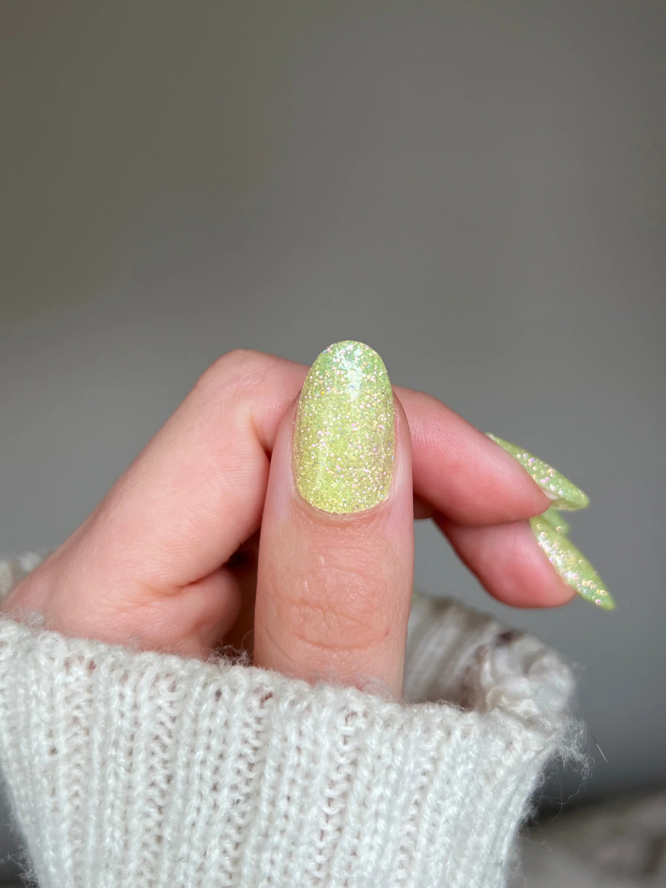 Een hand met lichtgroene glinsterende lemon fizz dipping powder op de nagels