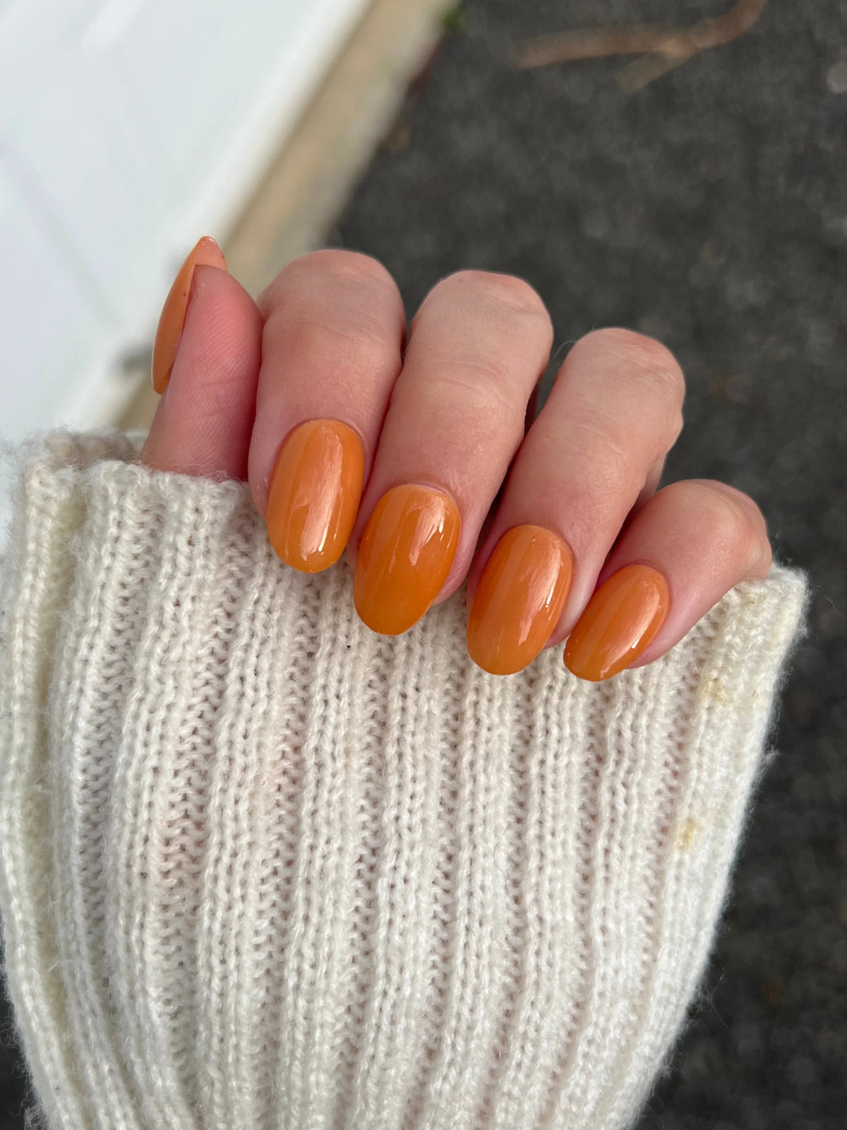 Hand met glanzende oranje nagellak gedaan met amber clay dipping powder voor duurzaam gebruik