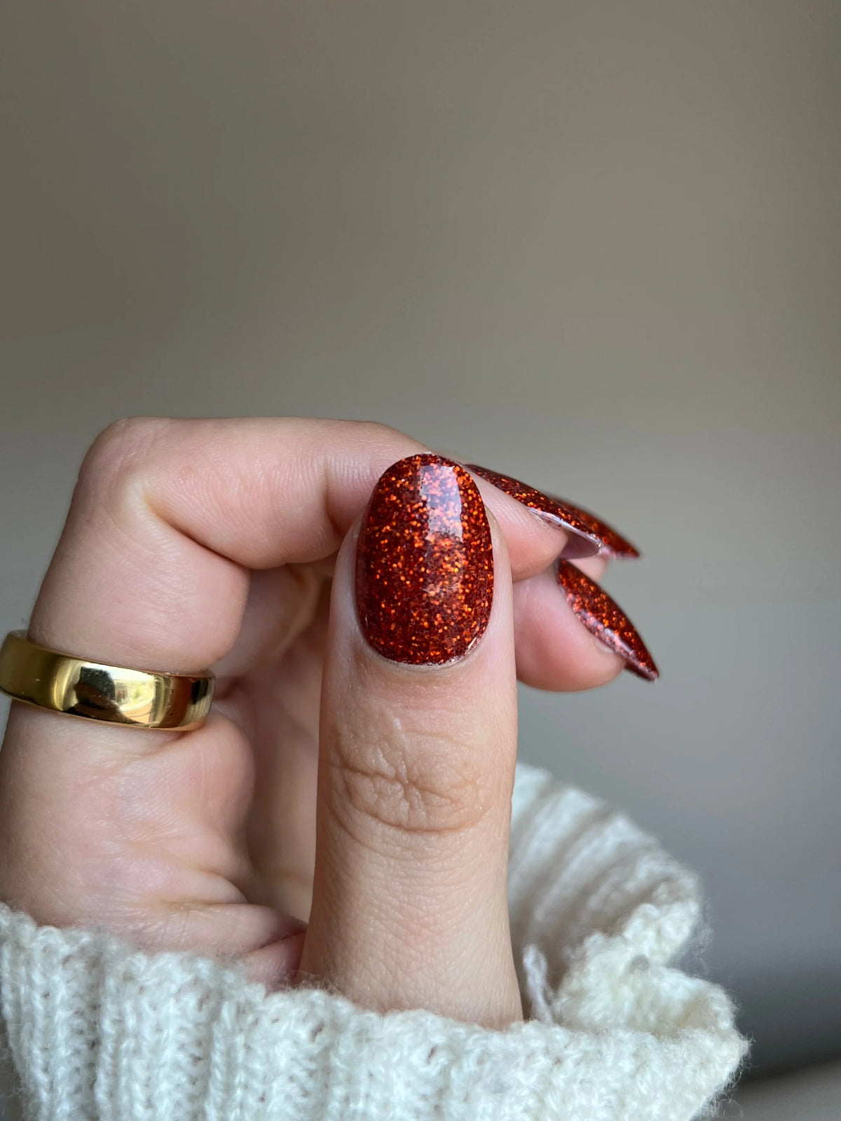 Hand met nagels in levendige glitterende rode copper sparkle dipping powder en een gouden ring