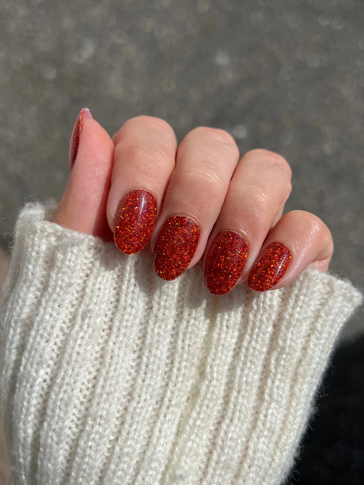Hand met copper sparkle dipping powder in levendige rode glitter met glanzende finish op een creme gebreide trui