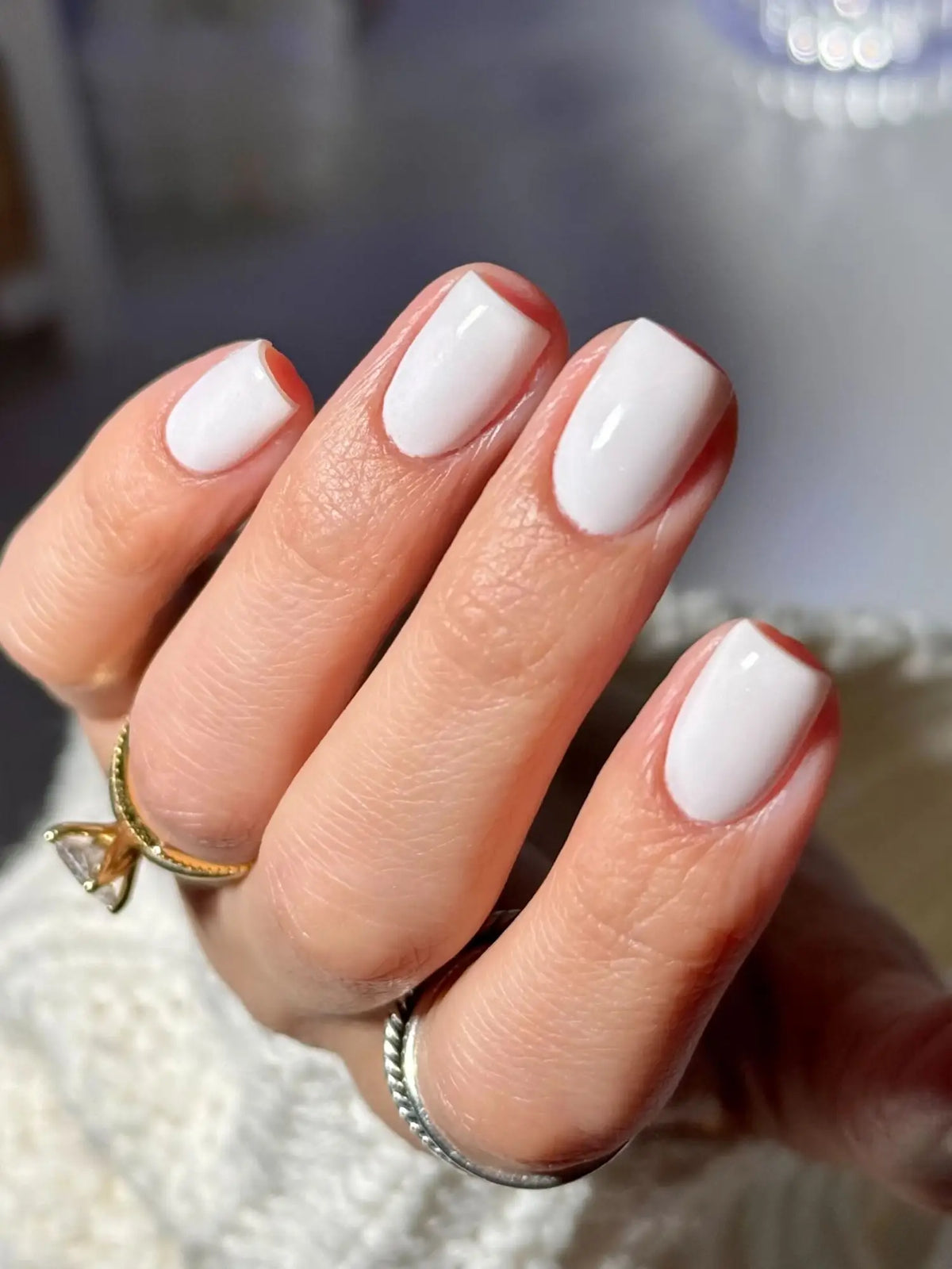 Hand met glossy witte biab nagels en twee ringen van diamant en gedraaid zilver illustreren verschillen met dipping powder