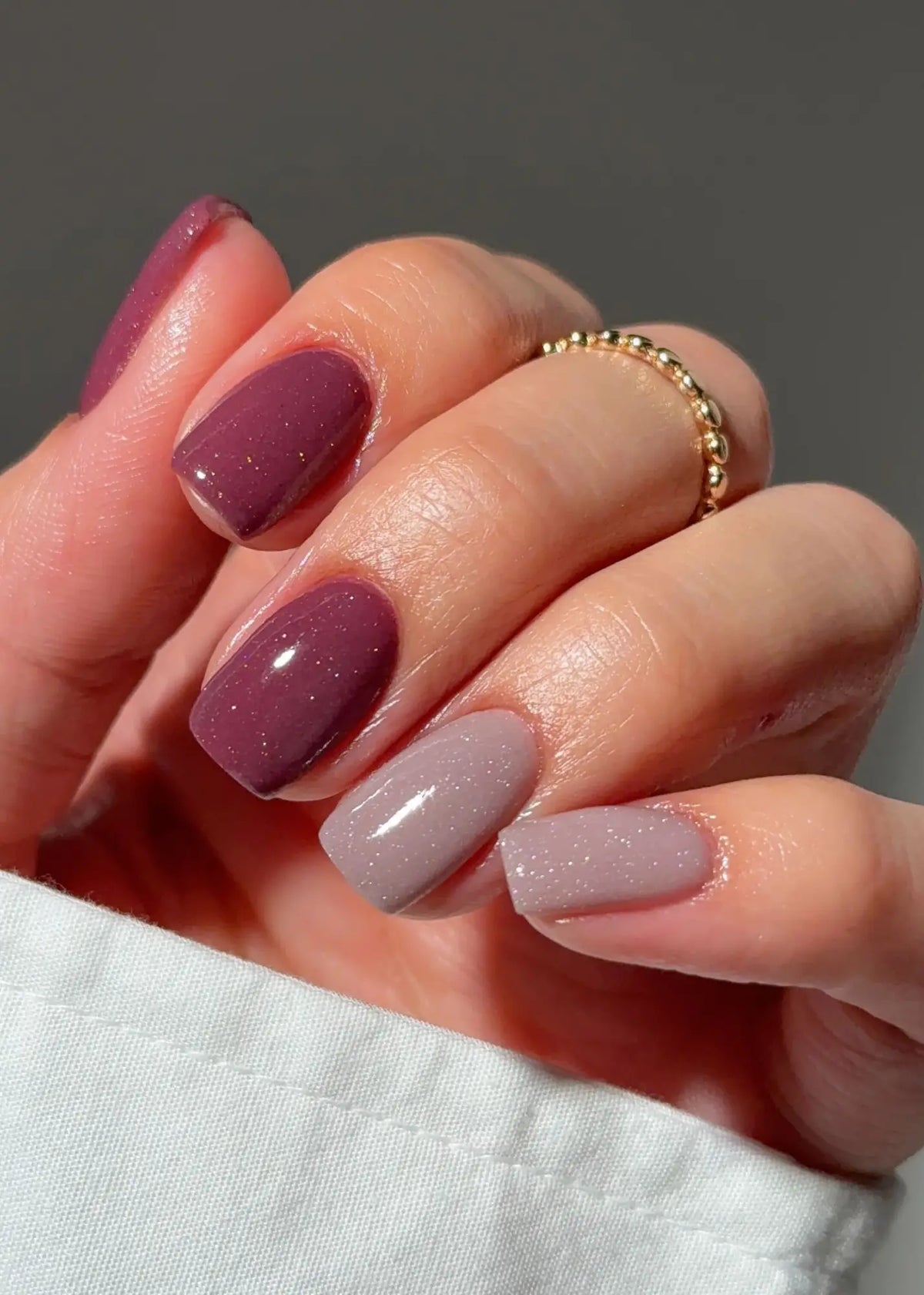Een hand met netjes gelakte nagels in een verloop van diep paars naar zacht lavendel met subtiele glitter voor nagelgroei met dipping powder