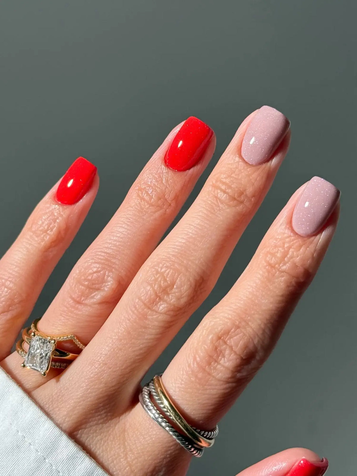 Een hand met nagels gelakt in levendig rood en zacht roze met glanzende afwerking en subtiele glitters voor nagelpoeder uitleg