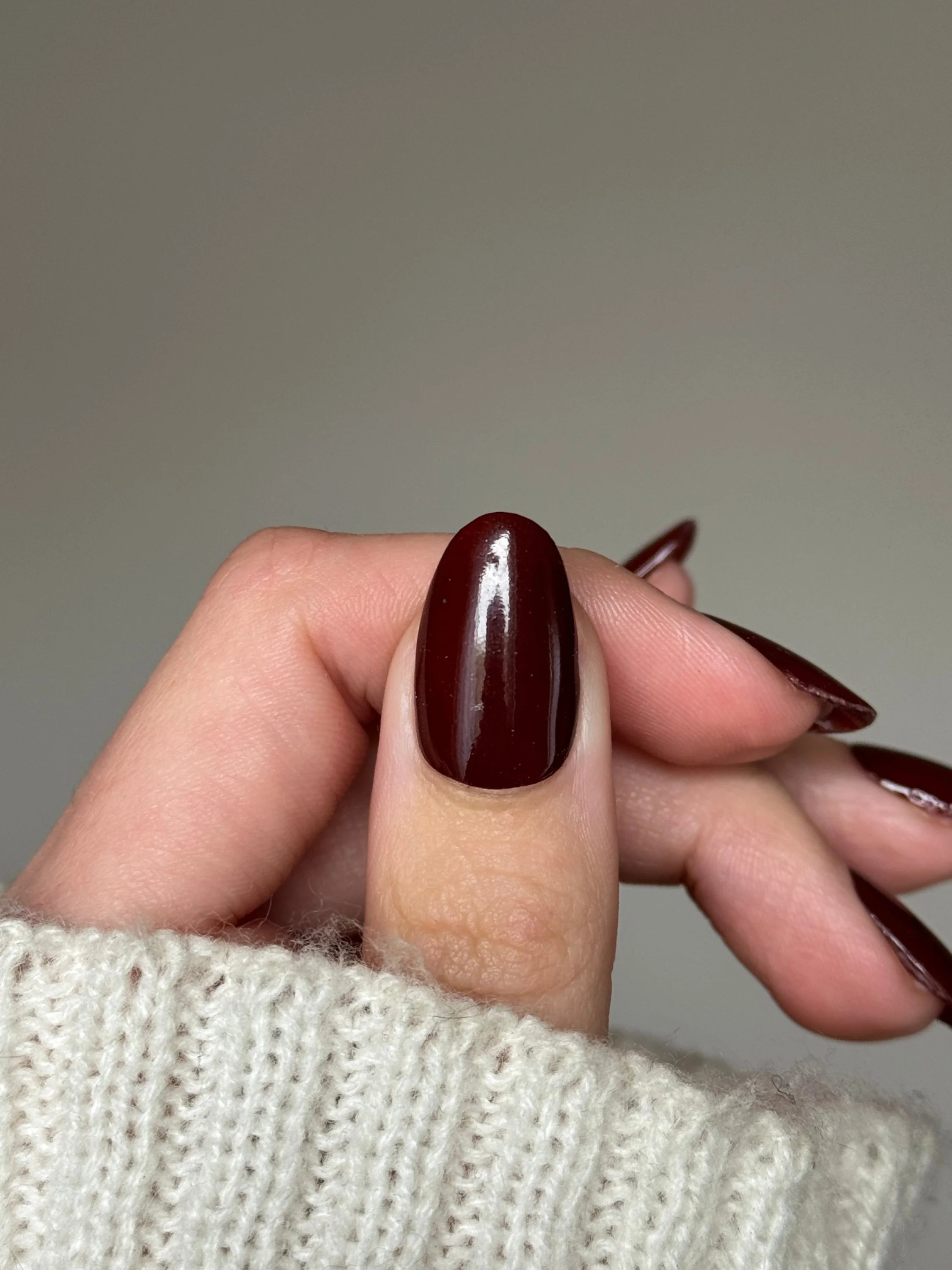 Een hand met lange amandelvormige nagels geverfd in glanzende diep bordeauxrode dip poeder dark chocolate