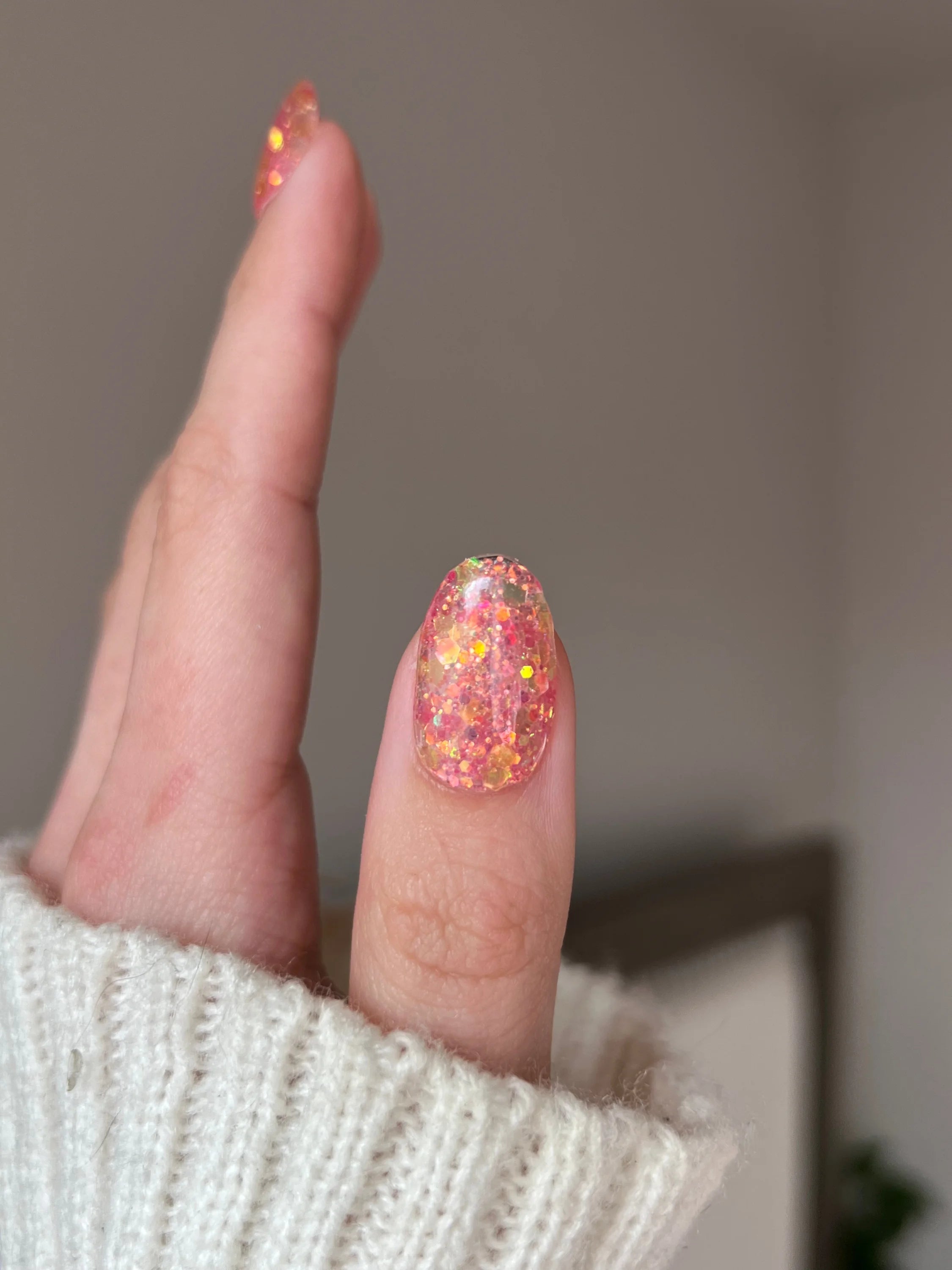 Een hand met een vinger met nagel gelakt in gouden roze dipping powder glanzende roze en oranje glitter