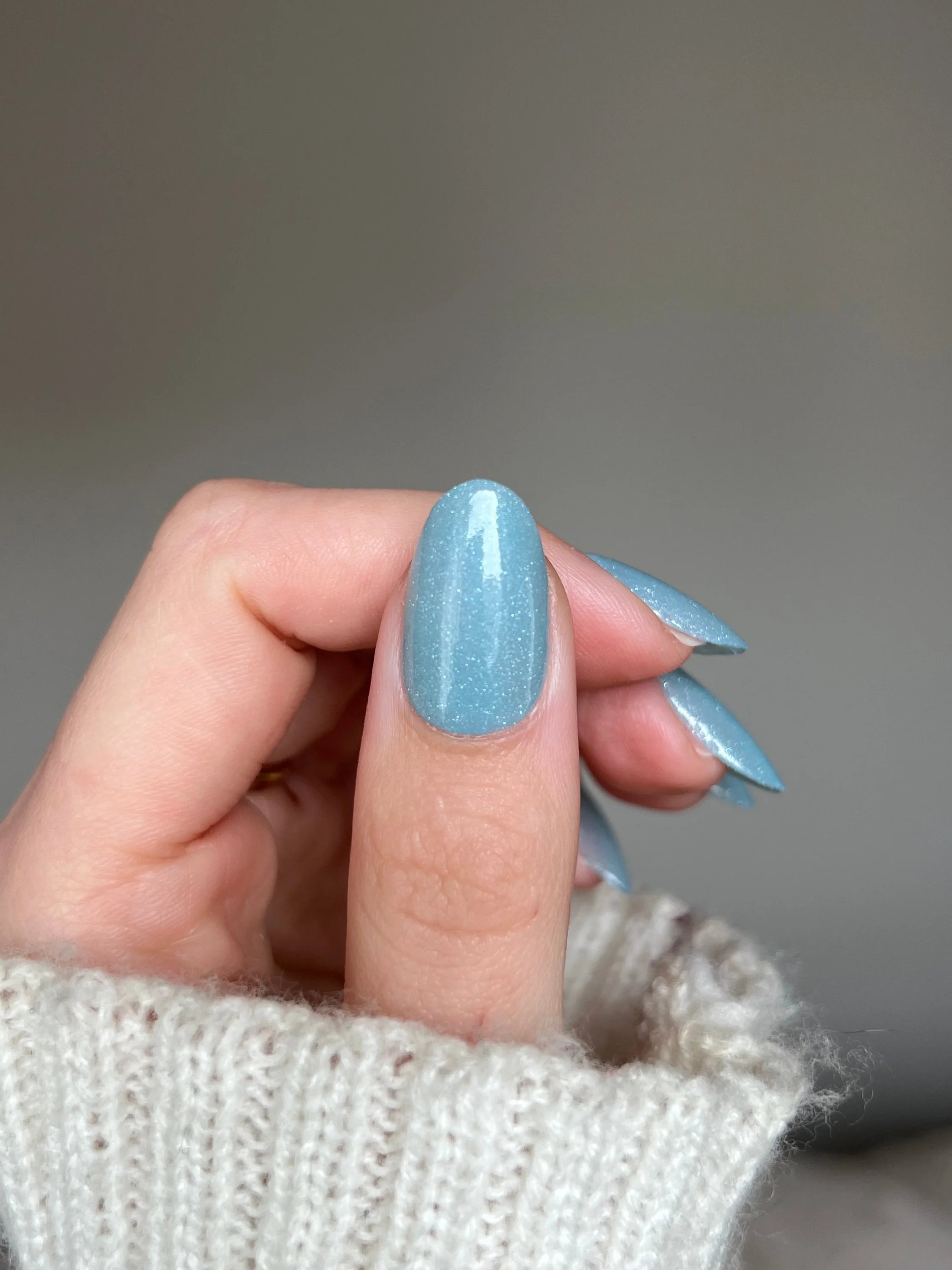 Een hand met lange amandelvormige nagels gelakt met glinsterende lichtblauwe mystic lagoon dipping powder