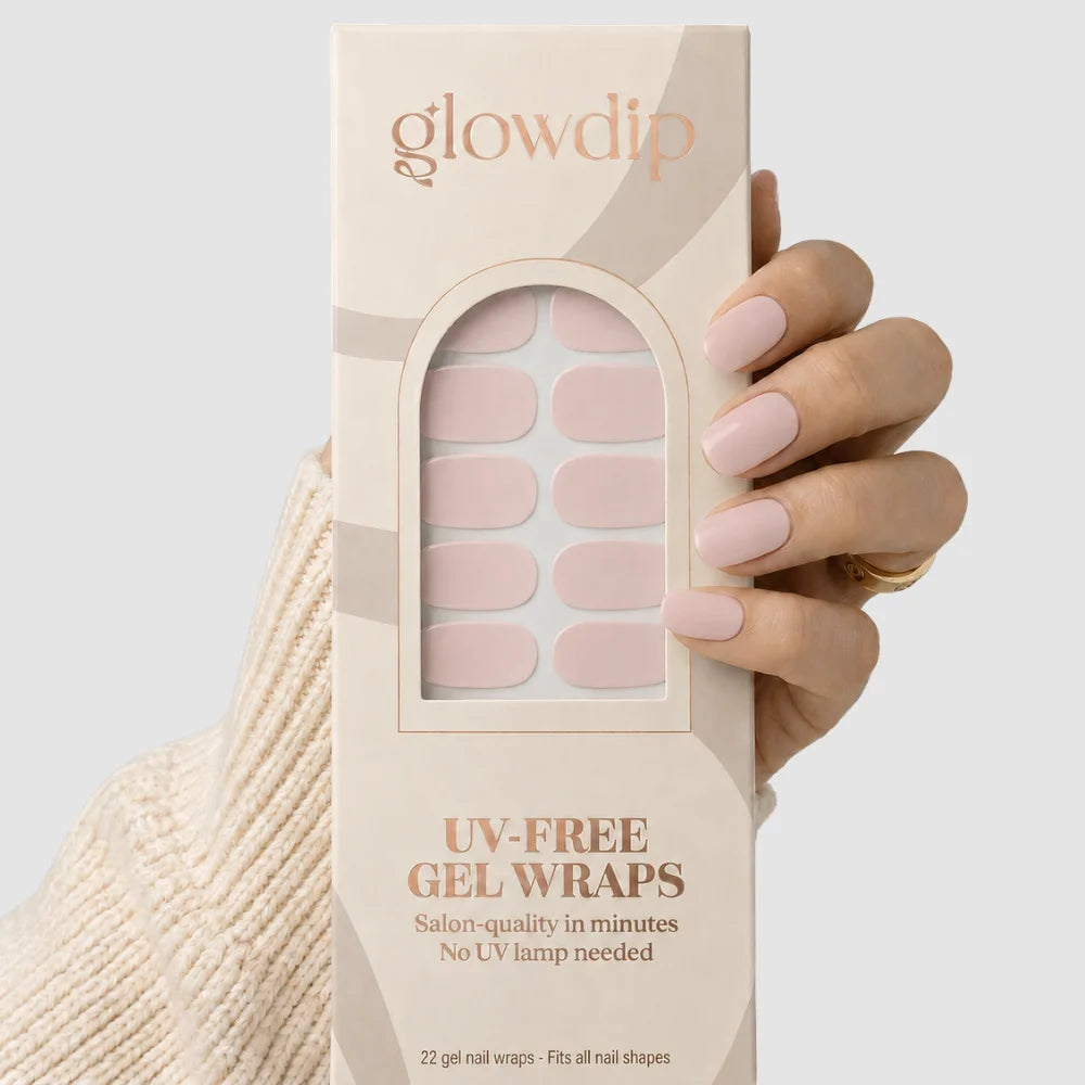 Een hand houdt een doos glowdip uv-free gel wraps met zachte roze nageldecal in een arched window beige verpakking