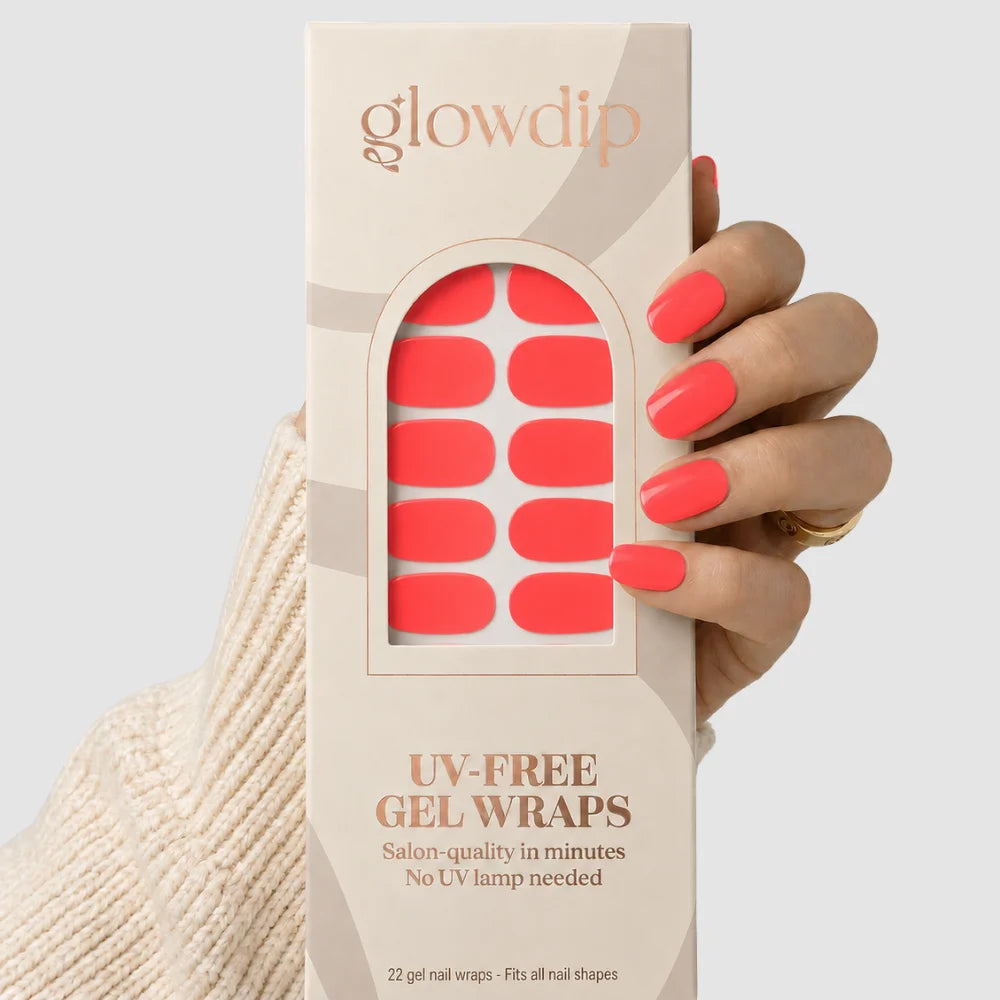 Een hand houdt een doos glowdip uv-vrije gel nagelwraps in zonsondergang koraal met salonkwaliteit