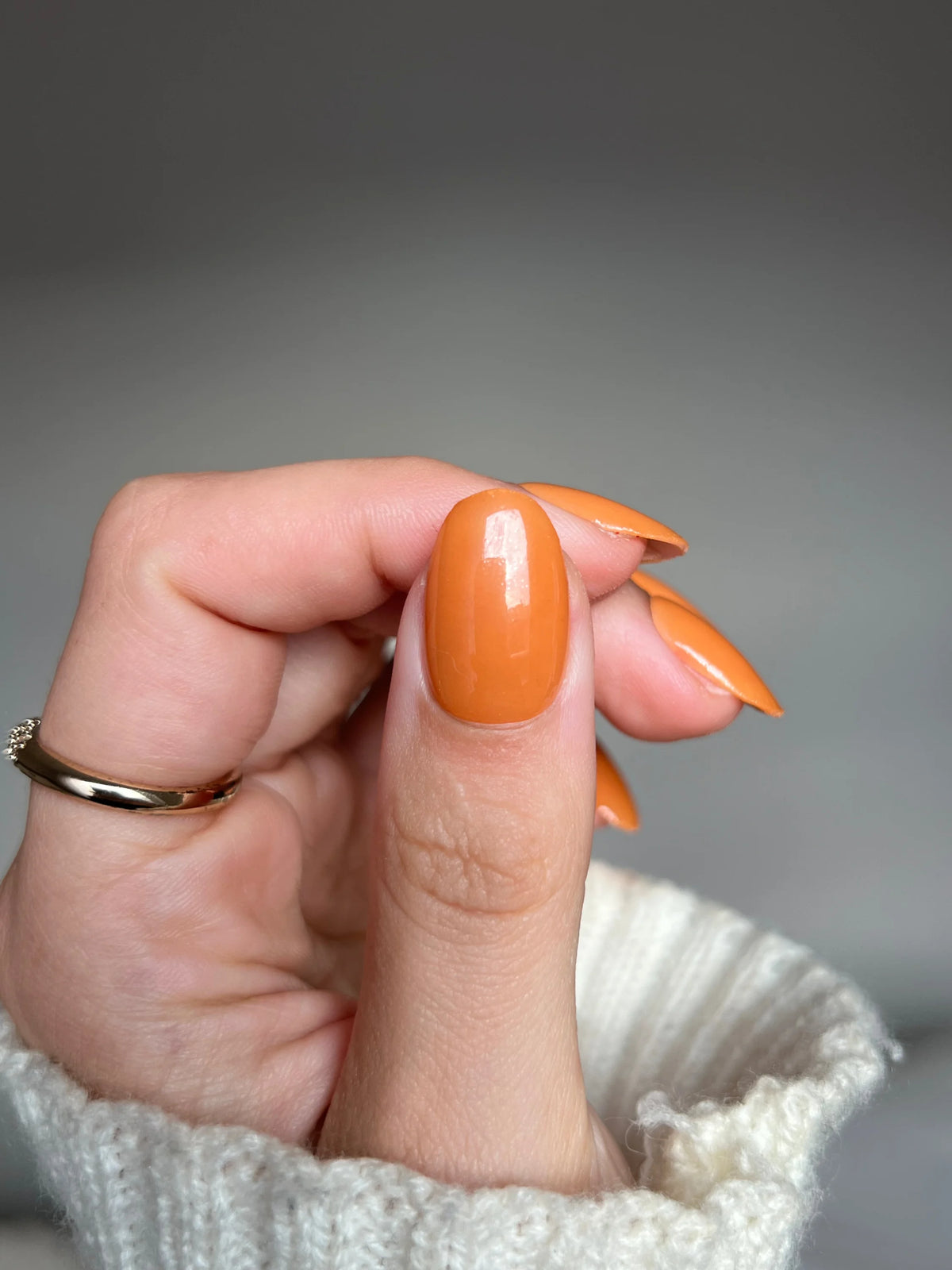 Een hand met lange glanzende oranje nagels en een eenvoudige gouden ring met amber clay dipping powder