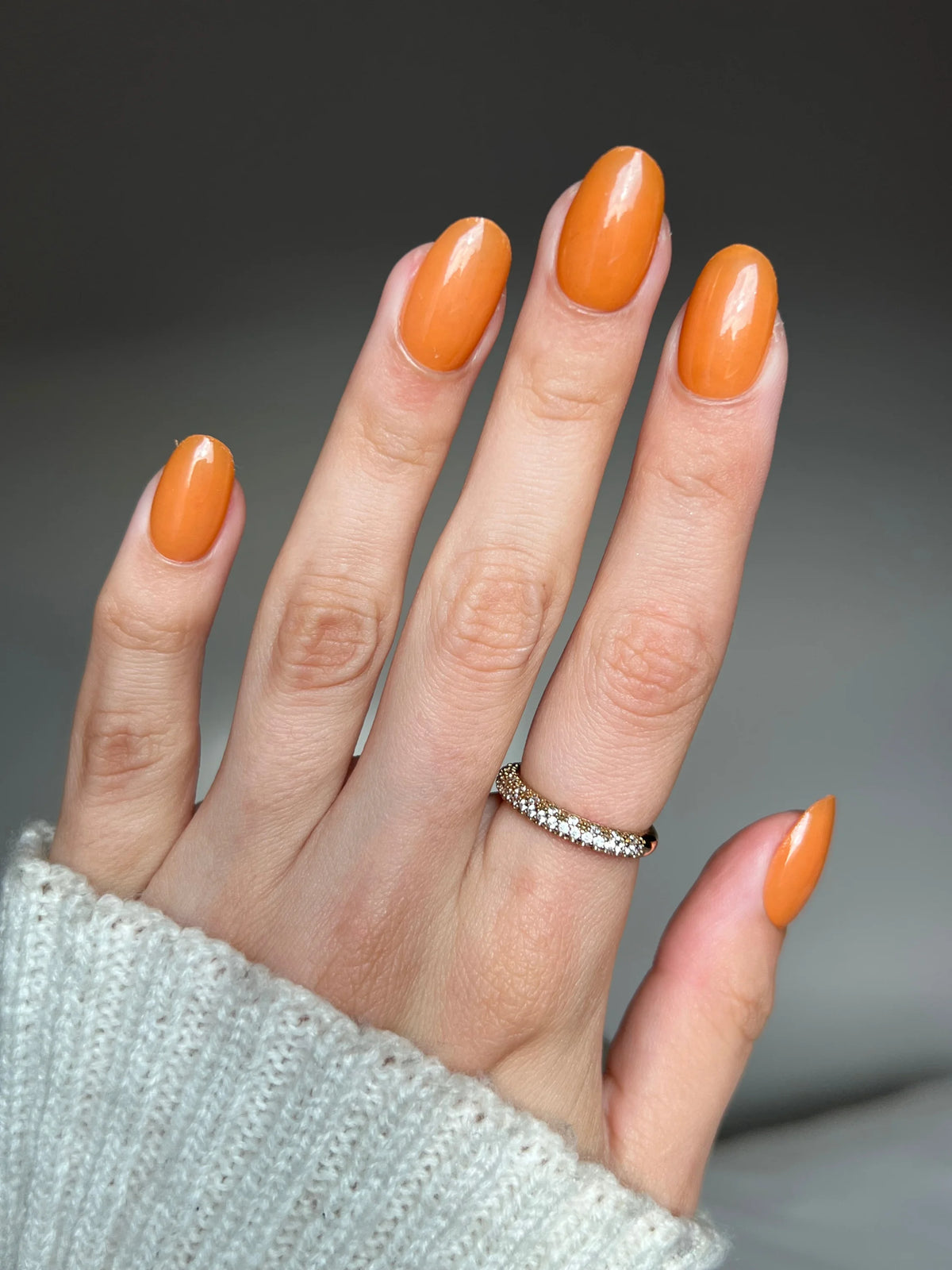 Hand met lange ovale nagels gelakt in glanzende oranje amber clay dipping powder en een delicate diamanten ring