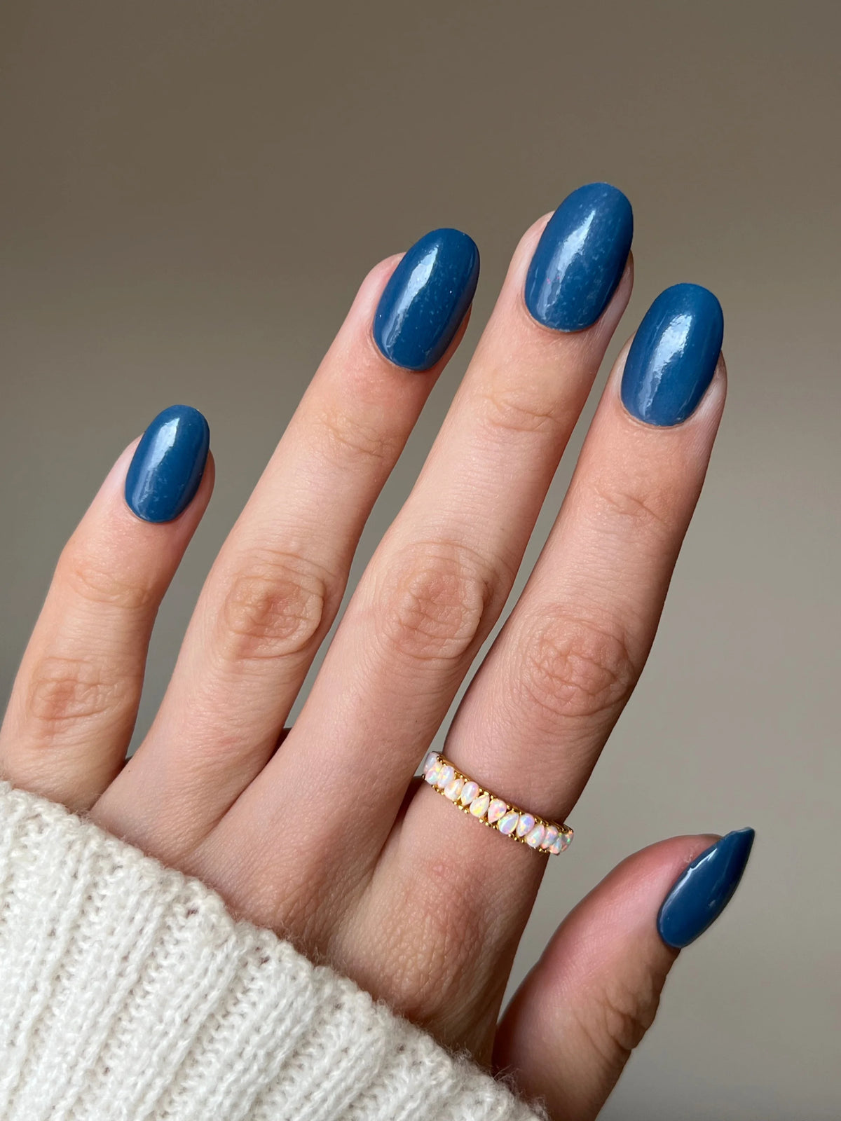 Een hand met lange ovalen nagels gelakt in glanzende diepe blauwe limited edition 10 moon glow dipping powder met een delicate gouden ring met kleine witte stenen
