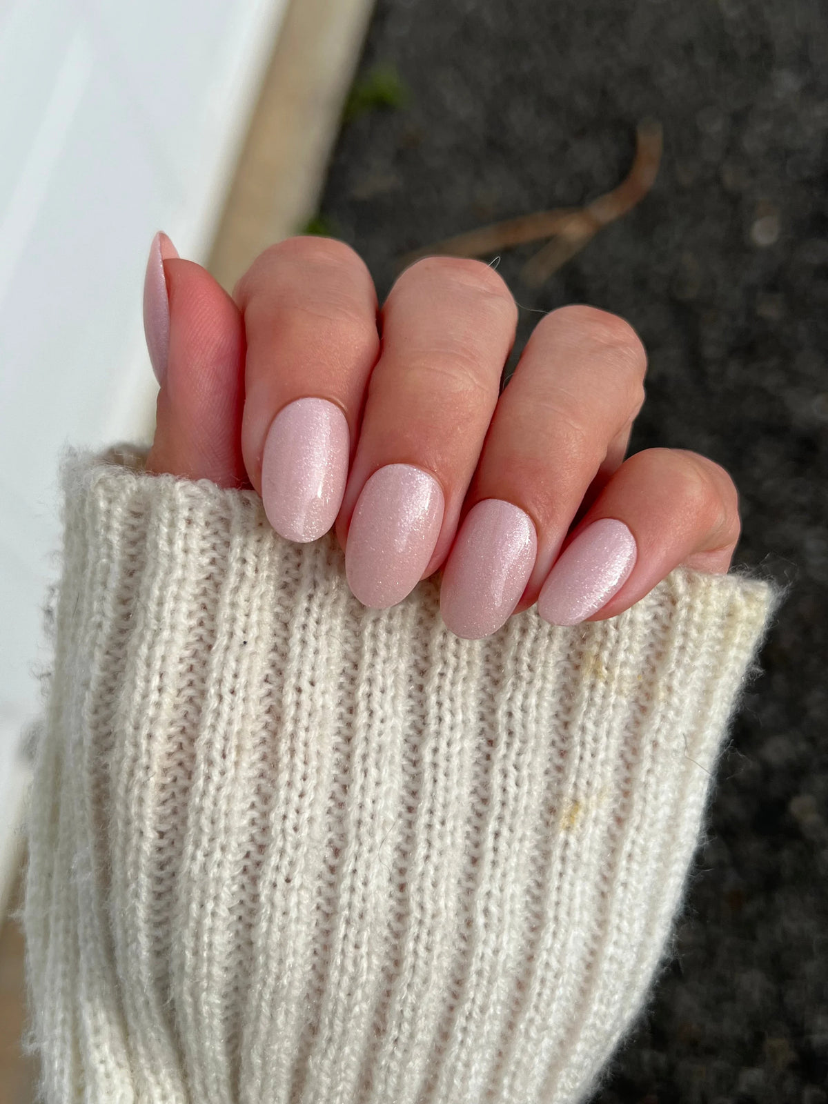 Hand met lange amandelvormige nagels in zachte roze nude glitter Silk Veil dipping powder met off-white trui